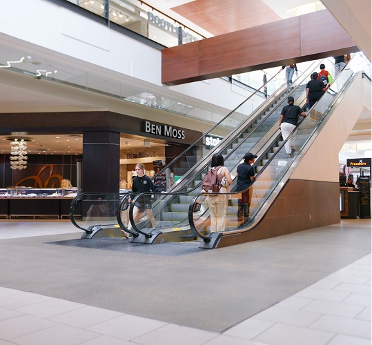 Shoppers riding escalators between mall levels near a Ben Moss store